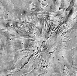 Tyrrhenia Patera on Mars (~200 km diameter). This is a flatter cone than Ceraunius and Uranius Tholus, but is thought to be composed of horizontally bedded ash deposits. The caldera and a flat-floored troughs merge into one another (MOC WA).