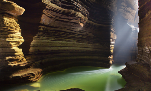 a green lake in a cavern with tall rock faces either side and the sun shining through the opening
