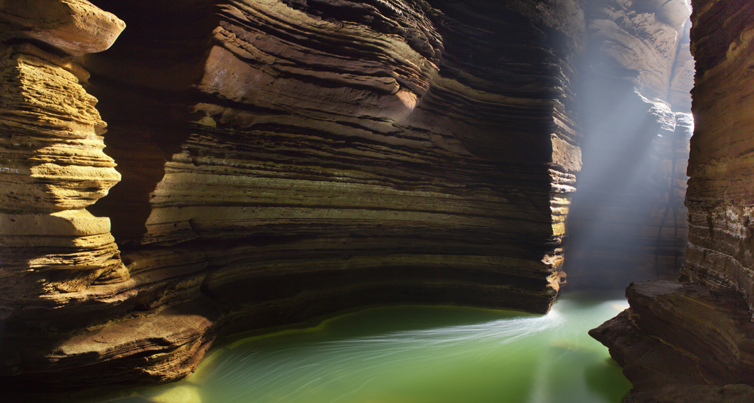 a green lake in a cavern with tall rock faces either side and the sun shining through the opening