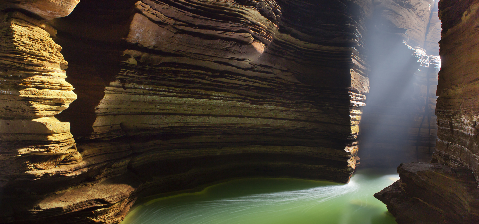a green lake in a cavern with tall rock faces either side and the sun shining through the opening