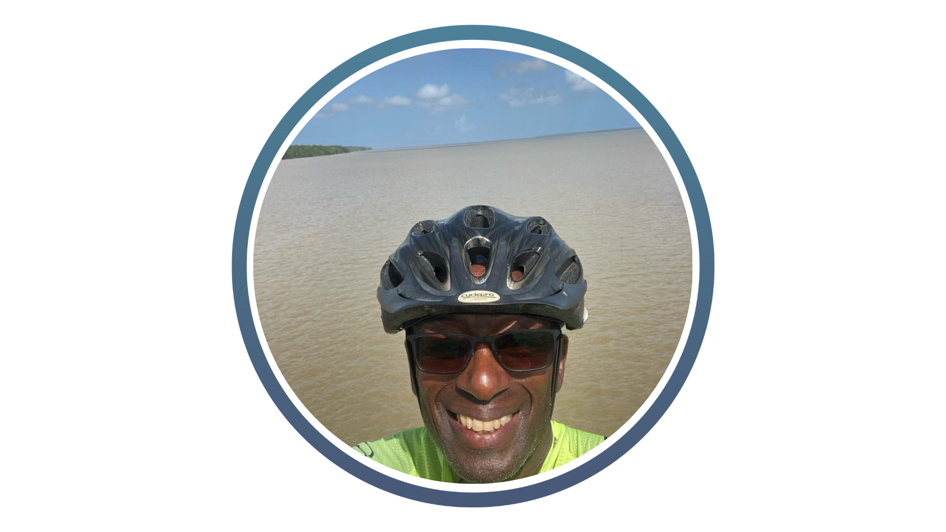Person wearing a bike helmet with a large body of water and distant greenery under a partly cloudy sky in the background.
