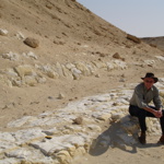 man wearing a cowboy hat sitting on rocks at the foot of a mountain