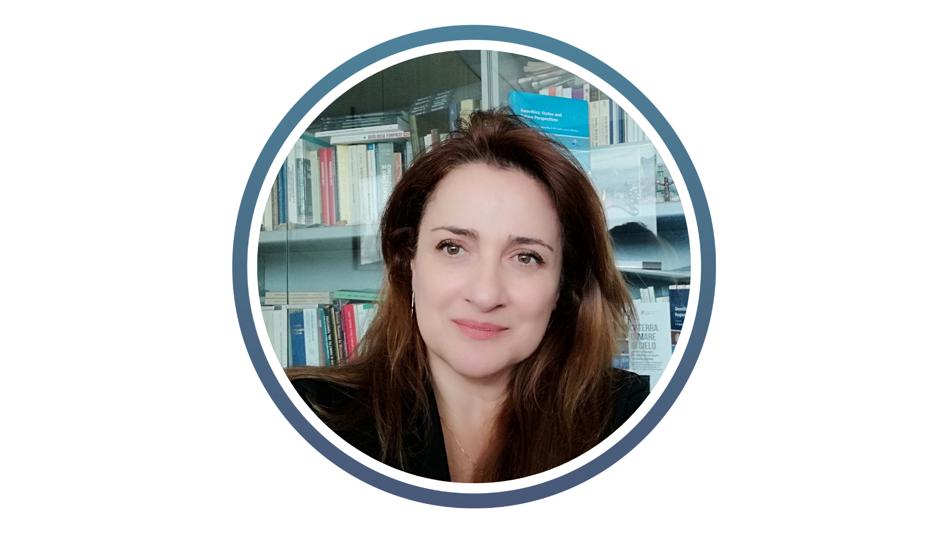 Person with long brown hair in front of a bookshelf filled with various books in an office or study setting.