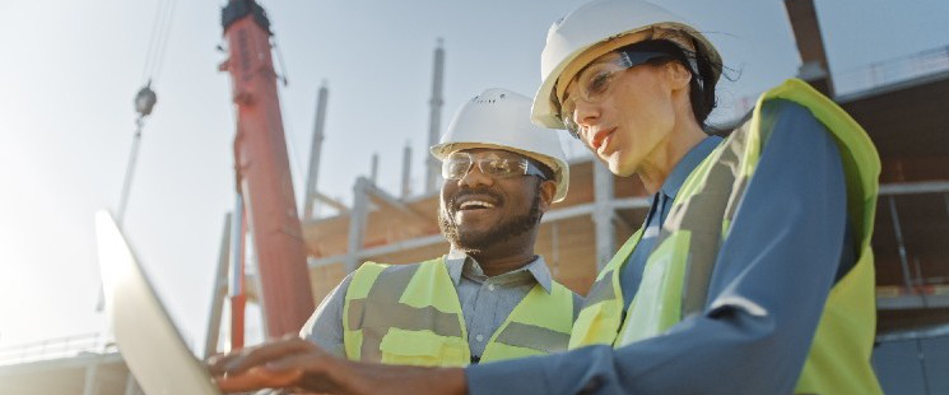 Two people in hardhats on site looking at a laptop