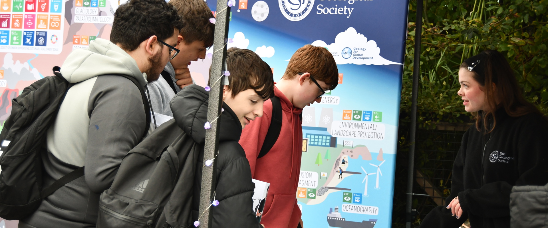 four young boys talking to a girl at a table which is full of badges and posters