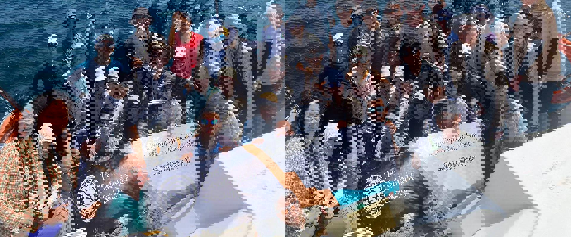 A group of people on a boat holding a banner with mountains and blue sky in the background