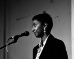 A black and white photo of a woman with short dark hair standing at a microphone