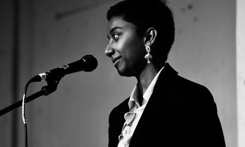 A black and white photo of a woman with short dark hair standing at a microphone