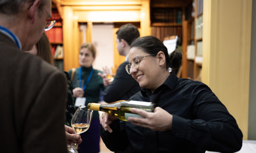 A server smiling while pouring white wine for a delegate in the Lower Library.