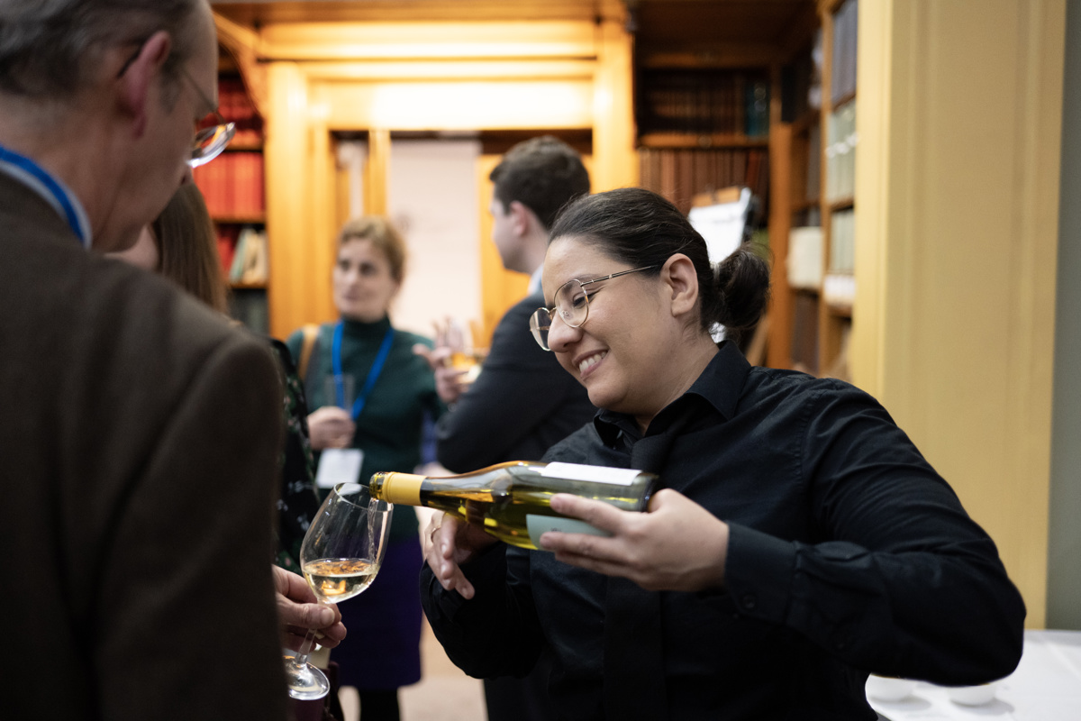 A server smiling while pouring white wine for a delegate in the Lower Library.