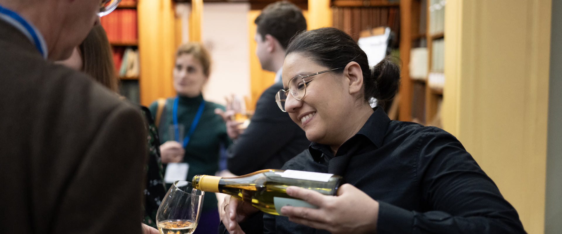 A server smiling while pouring white wine for a delegate in the Lower Library.