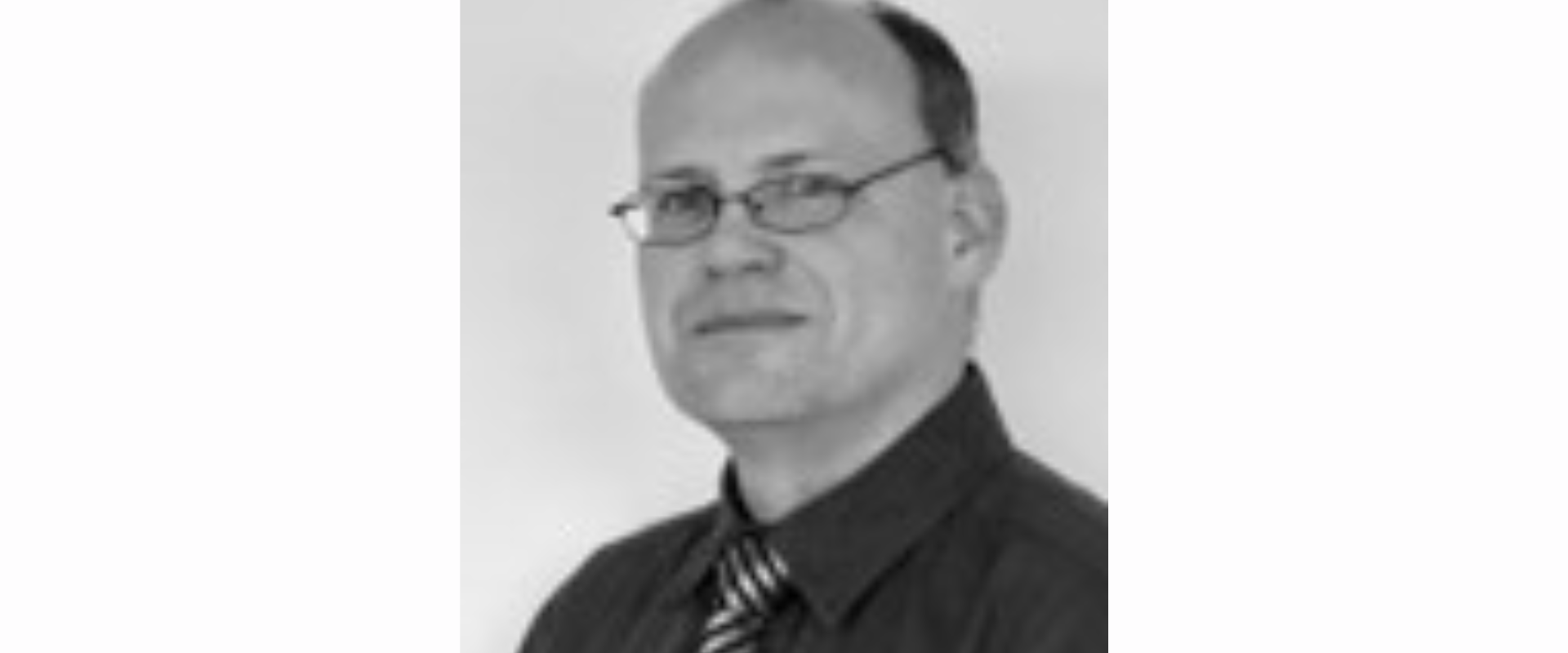 Black-and-white portrait of a person wearing glasses, a collared shirt, and a striped tie, positioned against a plain light background.