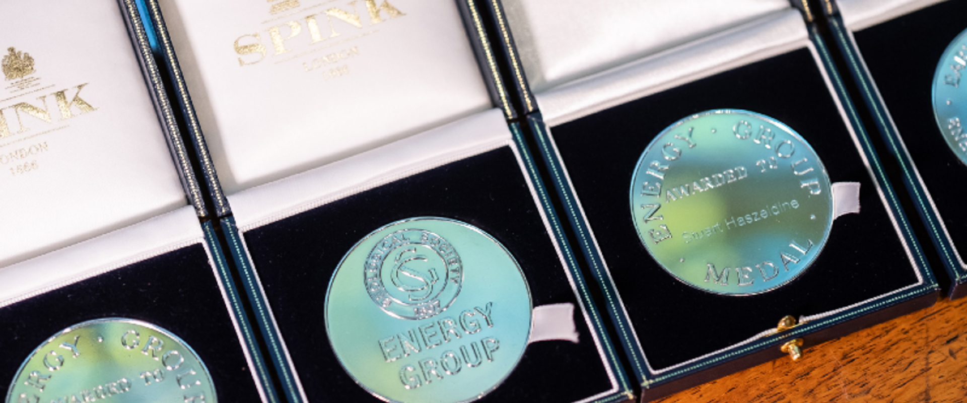 Four blue-hued medals displayed in elegant black boxes, each labeled "ENERGY GROUP MEDAL" and awarded to different individuals.