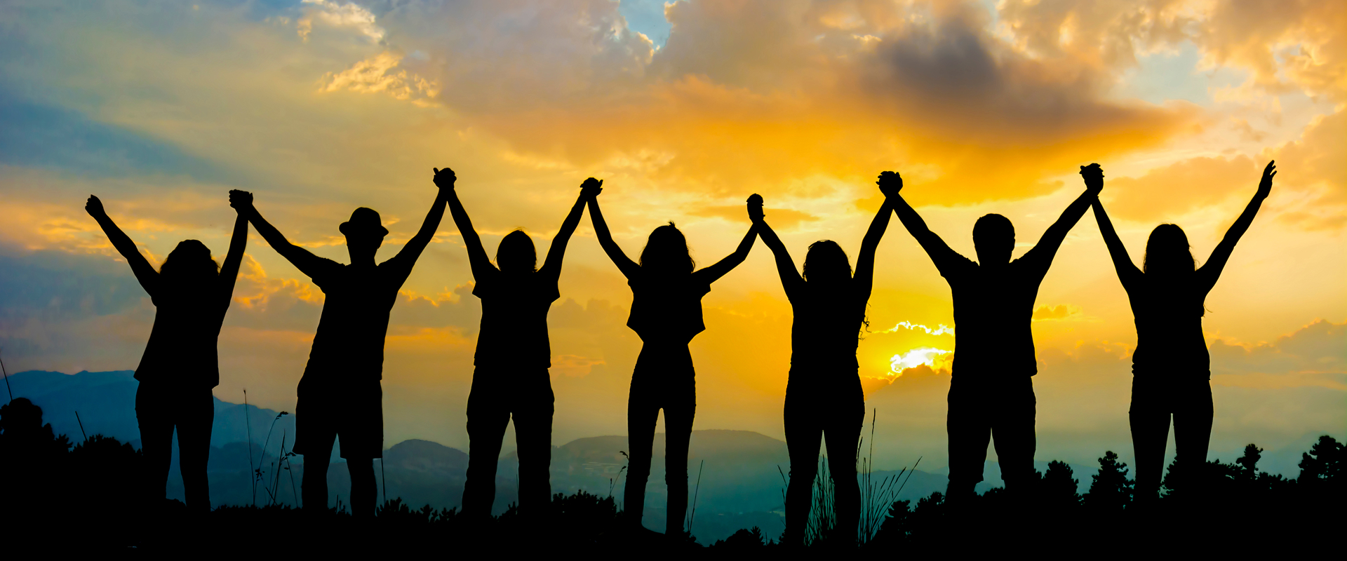 Silhouettes of a group of people holding hands with their arms in the air