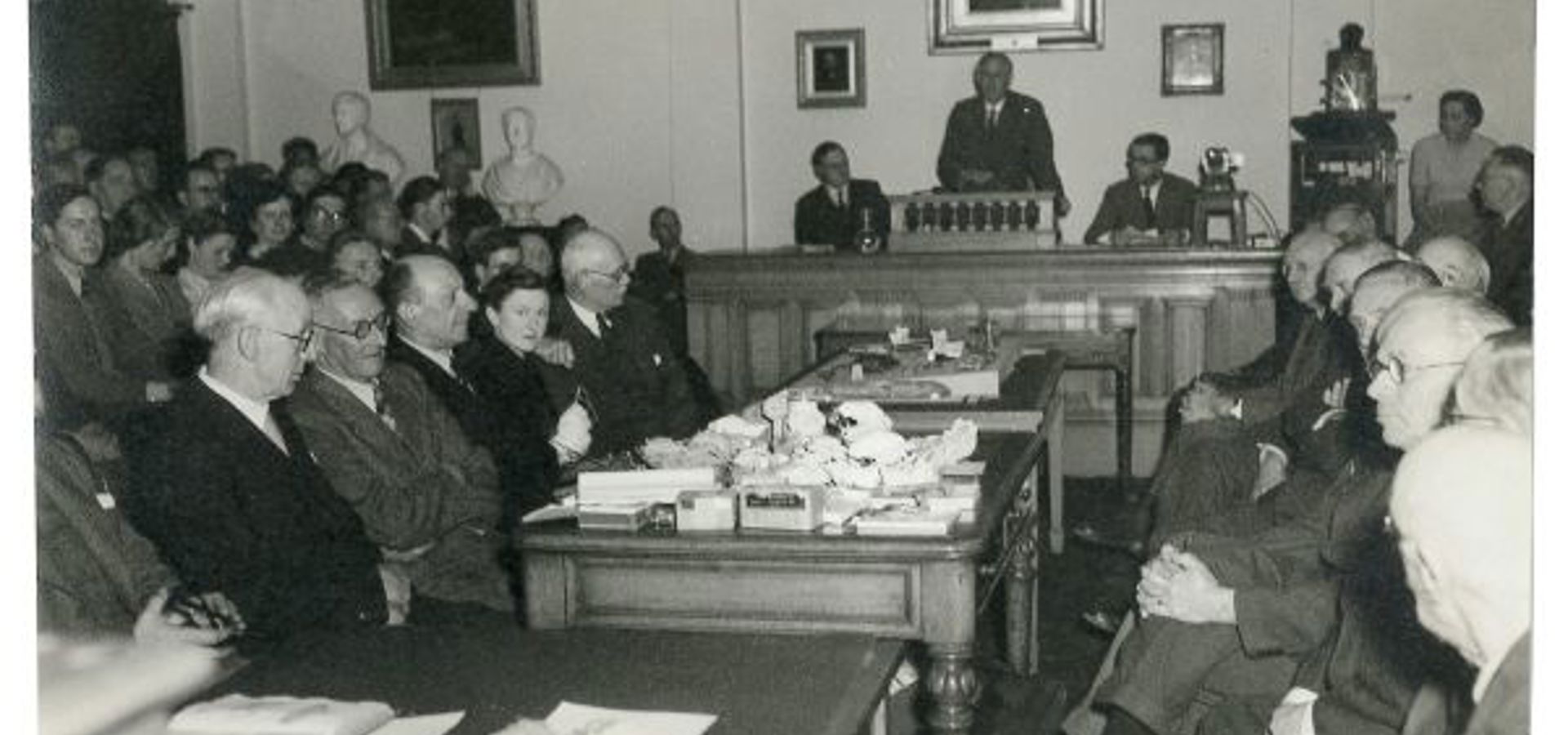 Old photograph of individuals seeting in a room facing each other durint a meeting