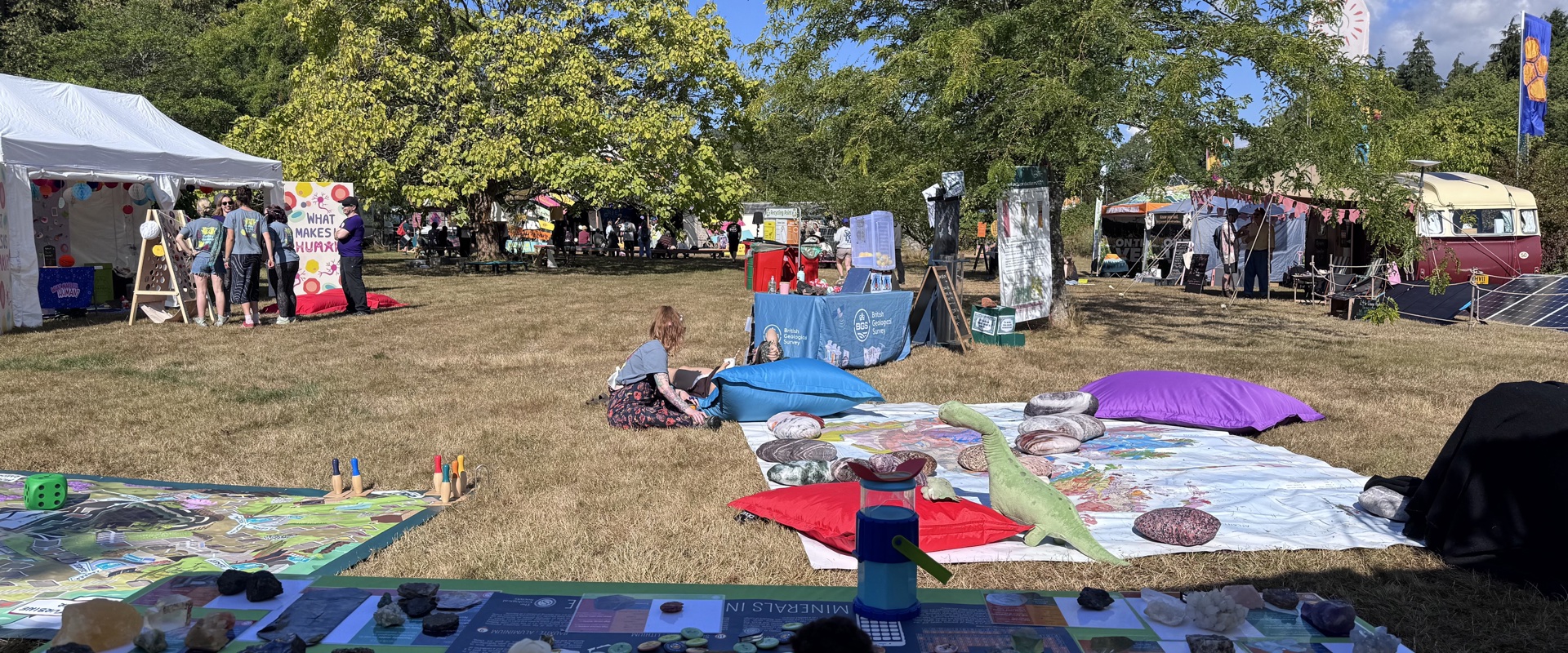 A table with minerls, informative posters and barbies in an open, green space during a festival