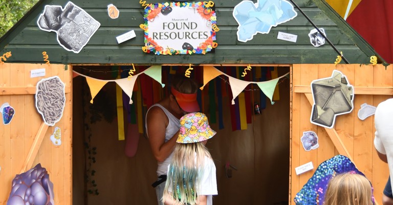 A girl walks into a decorated and colourful shed that reads Museum of Found Resources
