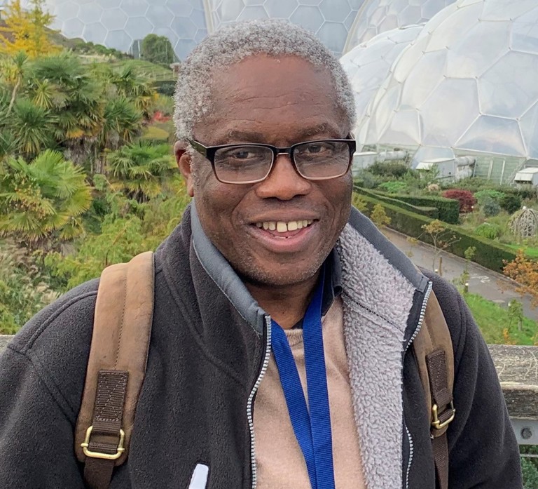 Black man with glasses wearing a fleece stood in front of some plastic domes