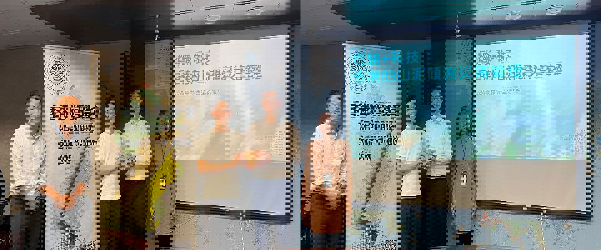 A group of professionals stands in front of a presentation about geological disaster management in Hong Kong, beside a banner of the Geological Society. 