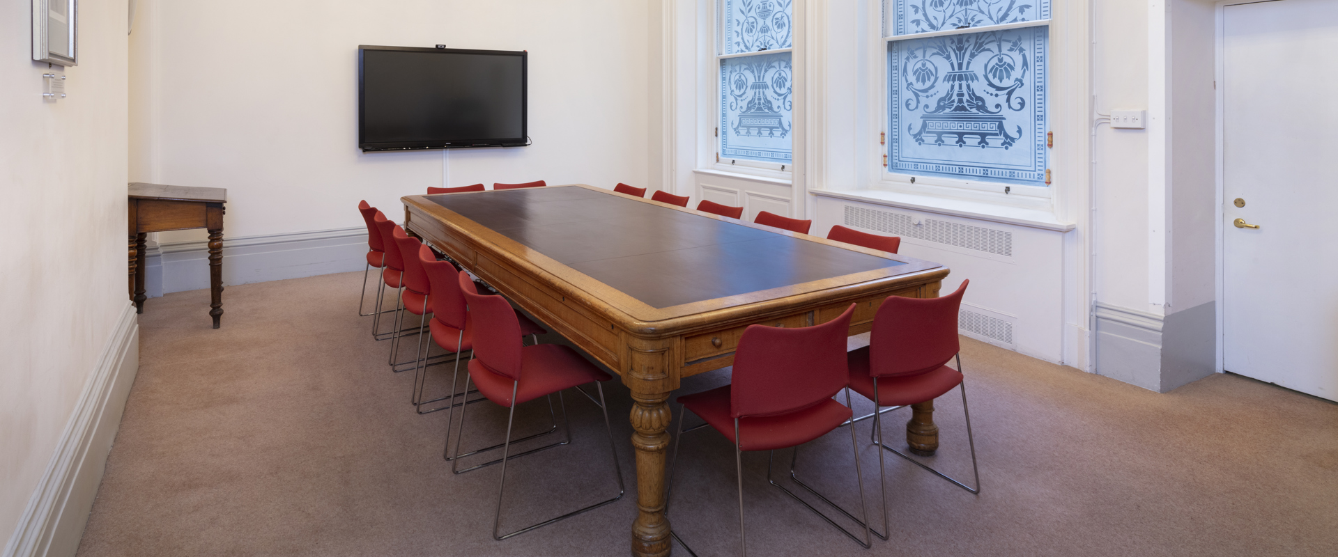 large table surrounded by red chairs and a tall window