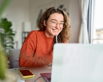 Young woman in glasses smiling at laptop with pen