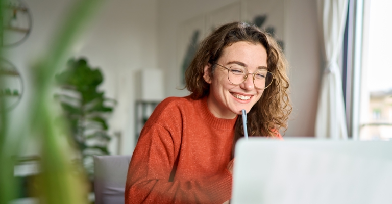 Young woman in glasses smiling at laptop with pen