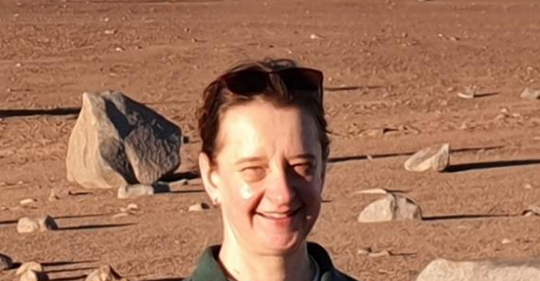 A woman standing in a desert wearing a green top and smiling at the camera