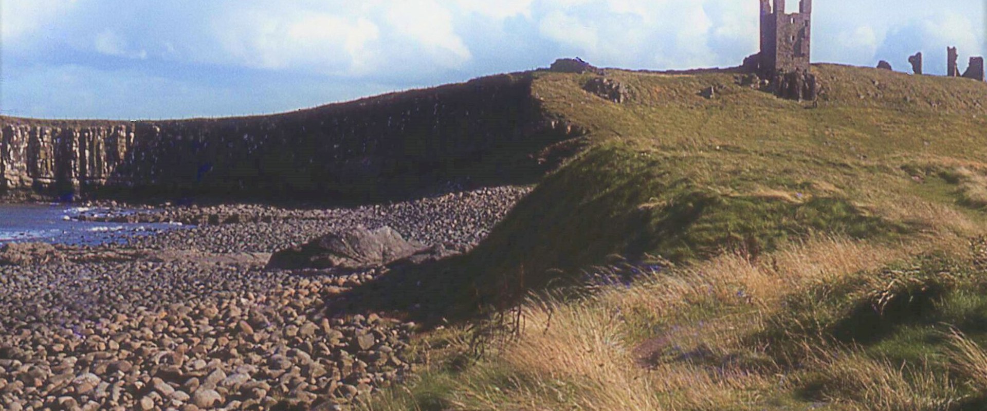 castle perched on a green hill with a sweeping cliff and a rocky beach in the foreground