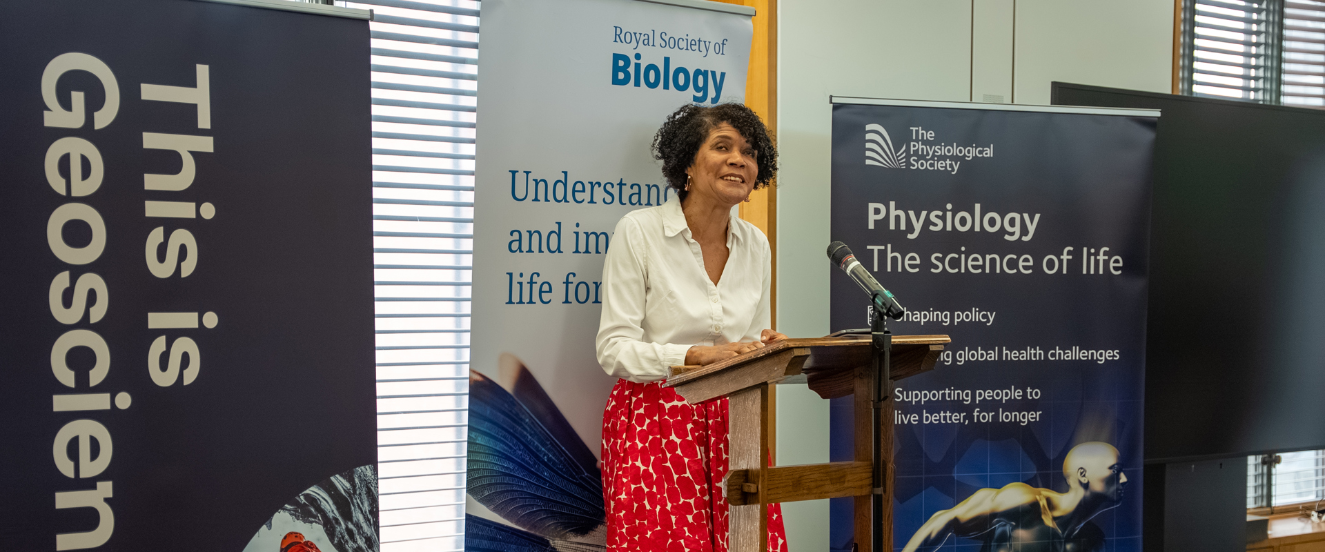 Dame Chi Onwurah MP standing in front of science-related roller banners ready to give a speech. 