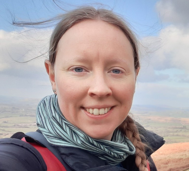 young woman with a plaited ponytail and stripy neck scarf stood in front of an open landscape