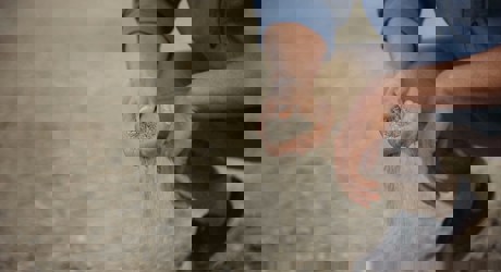 person crouching with sand falling through their fingers