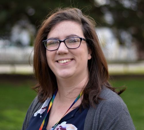 woman with long dark hair and glasses wearing a grey jacket and flowery blue shirt