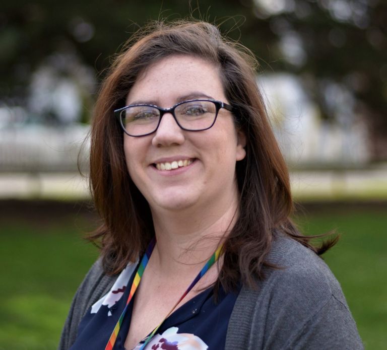 woman with long dark hair and glasses wearing a grey jacket and flowery blue shirt