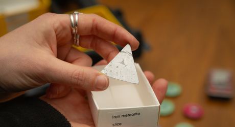 close up of a hand holding a triangular piece of iron meteorite