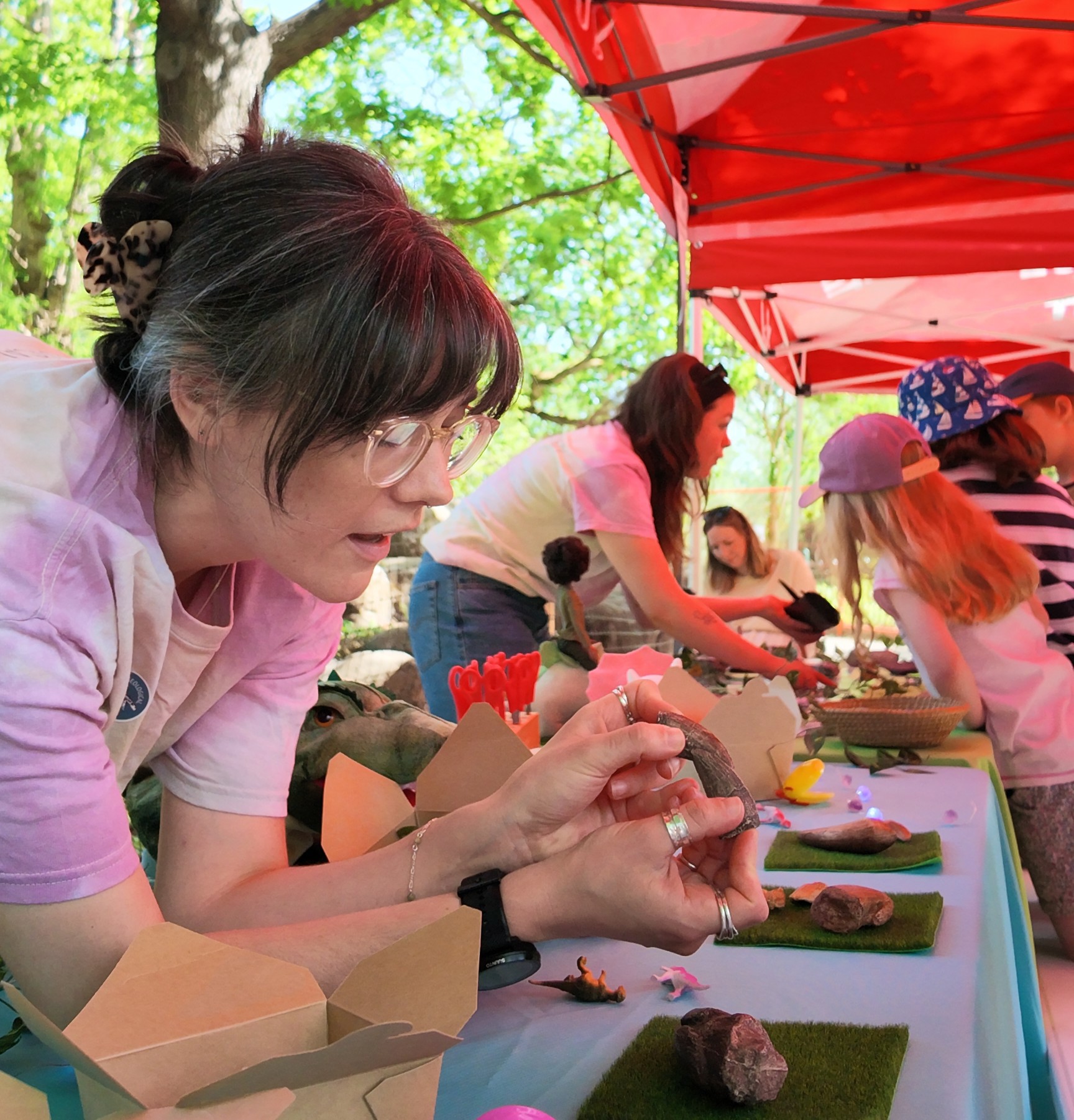 Woman showcasing two dinosaur teeth replica with more fossils on table