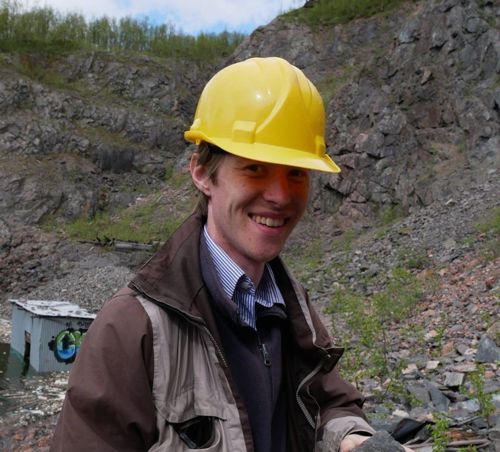 man wearing a yellow hard hat and brown jacket stood in front of a quarry