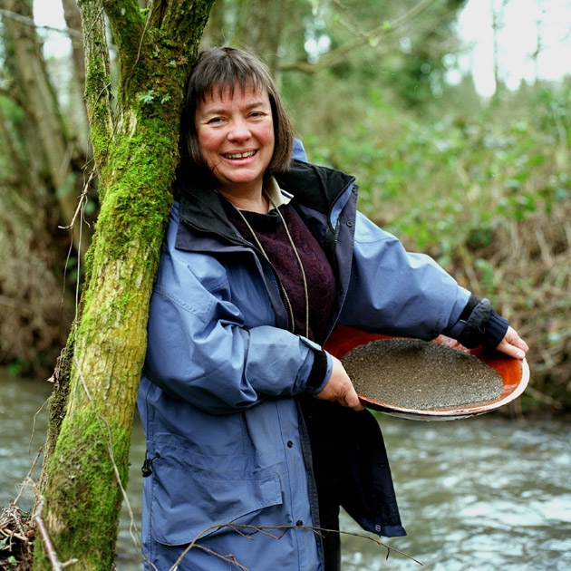 brown haired woman standing by a tree holding a bowl of sandy deposits