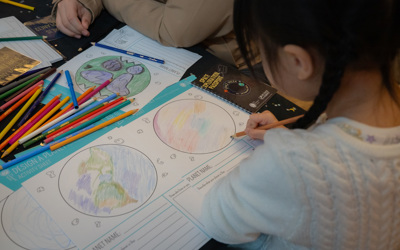 Young girl drawing in Earth and planet printed activity sheets with colour pencils. 