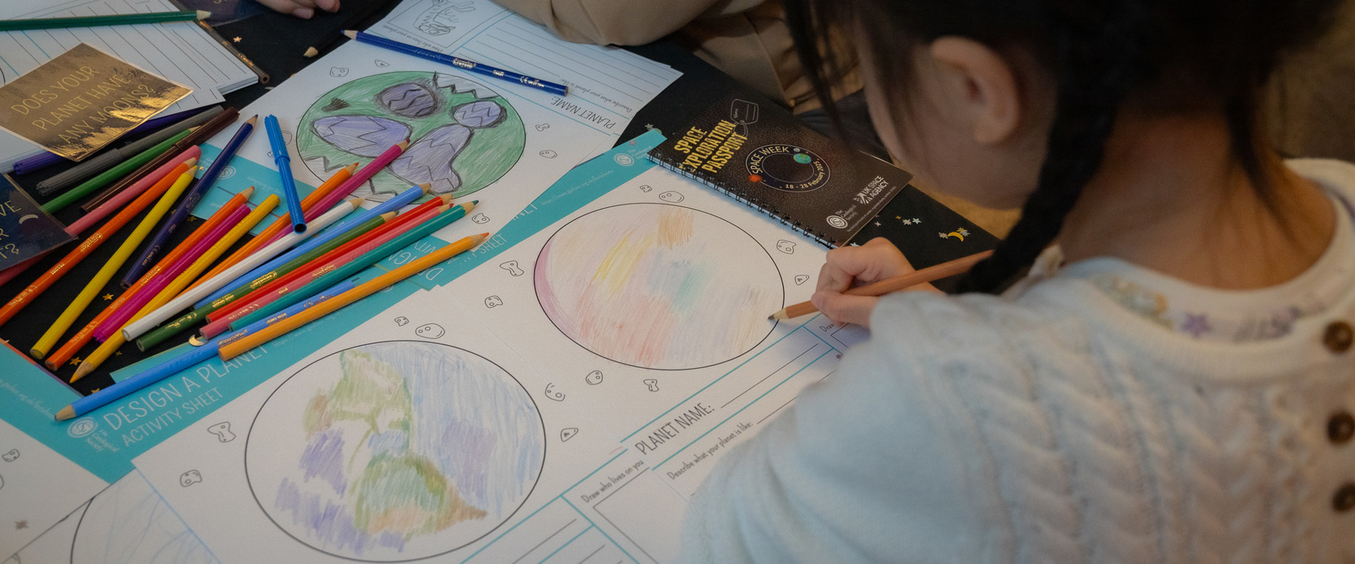 Young girl drawing in Earth and planet printed activity sheets with colour pencils. 