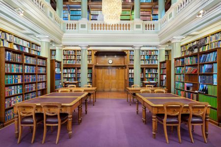 The Upper Library of the Geological Society of London, tables and chairs on a maroon carpet surrounded by book-lined shelves and green pillars