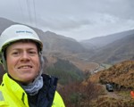 a white man with a hard hat and high vis jacket with mountain valley behind
