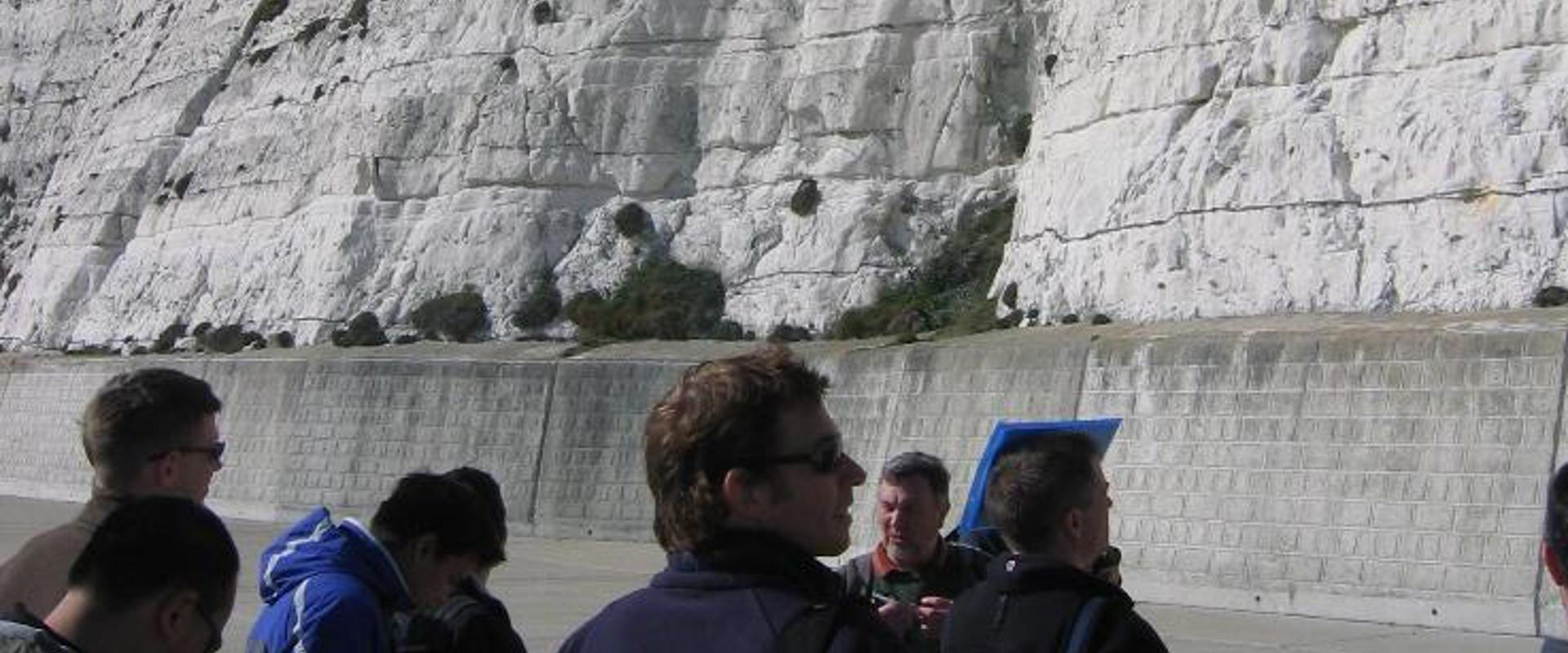 A group of people standing in front of a chalky cliff face with blue sky in the background