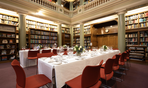 Long table sit-down dining setup in the Upper Library with a floral centrepiece and table cutlery.