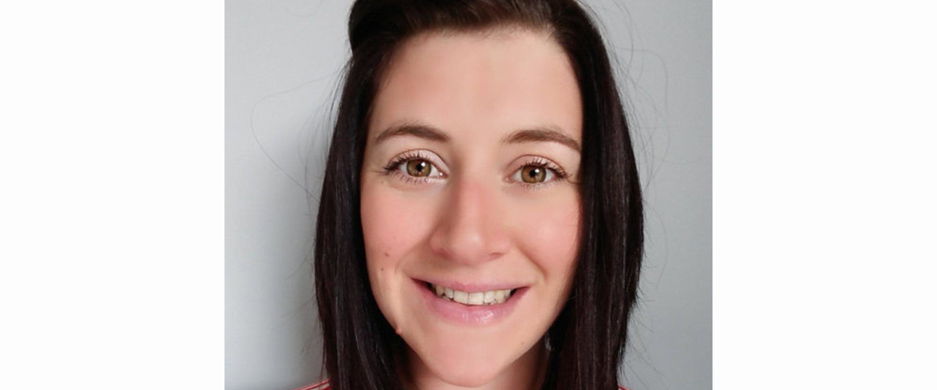 A person with straight, dark shoulder‑length hair, positioned against a plain light grey background. The individual is wearing a red and white striped top.