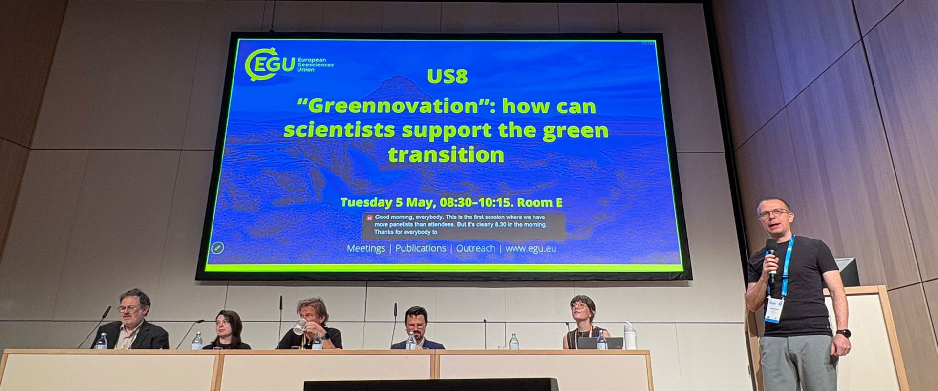 Panellists sit in front of a slide presenting a 'Greenovation' discussion