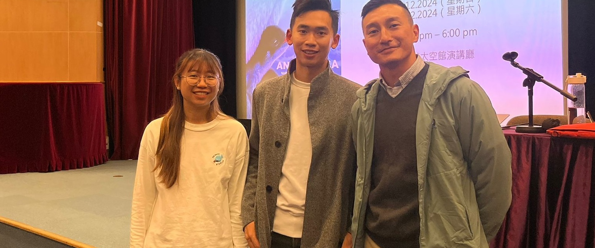 two males and one female stood in front of a screen with writing on it