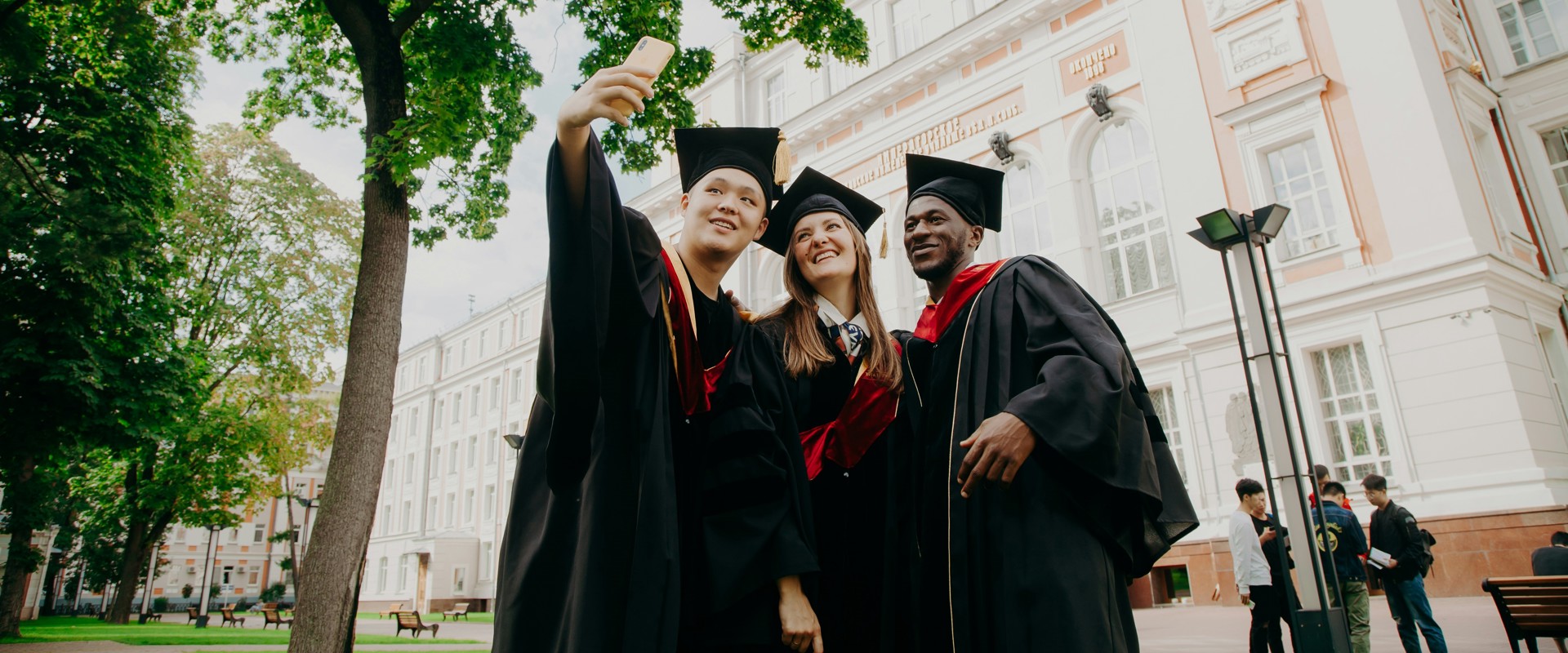 two women and one man in mortar boards and gowns smiling at a camera