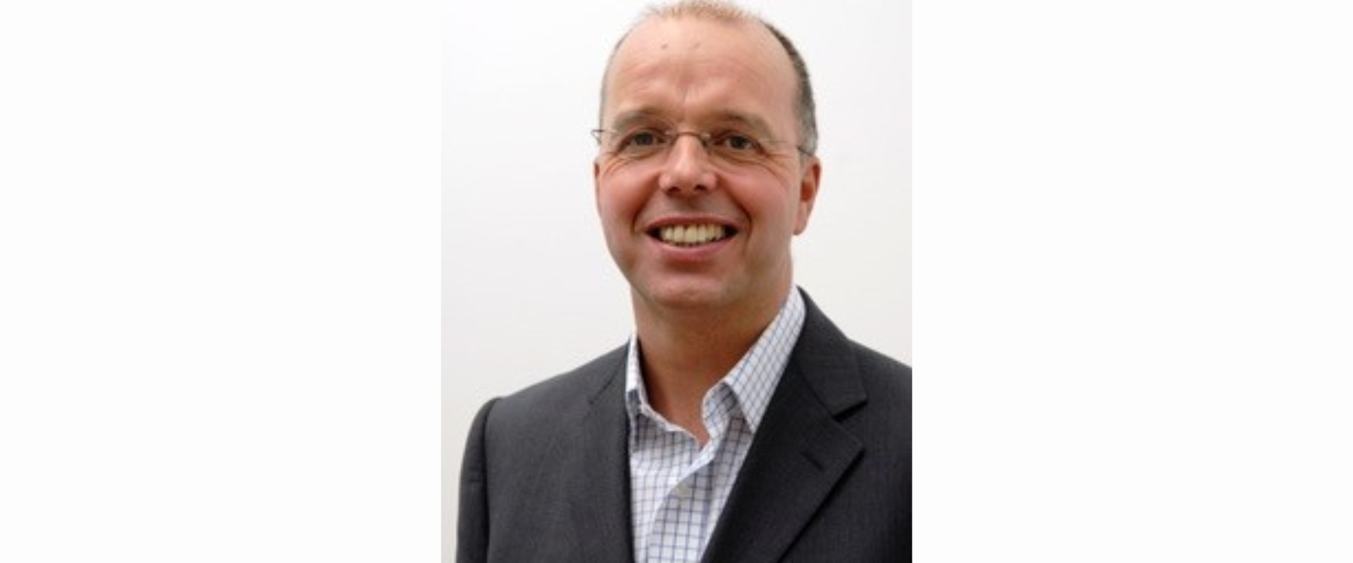 A person wearing a dark suit jacket over a light check-patterned shirt, shown from the torso upward against a plain light background.