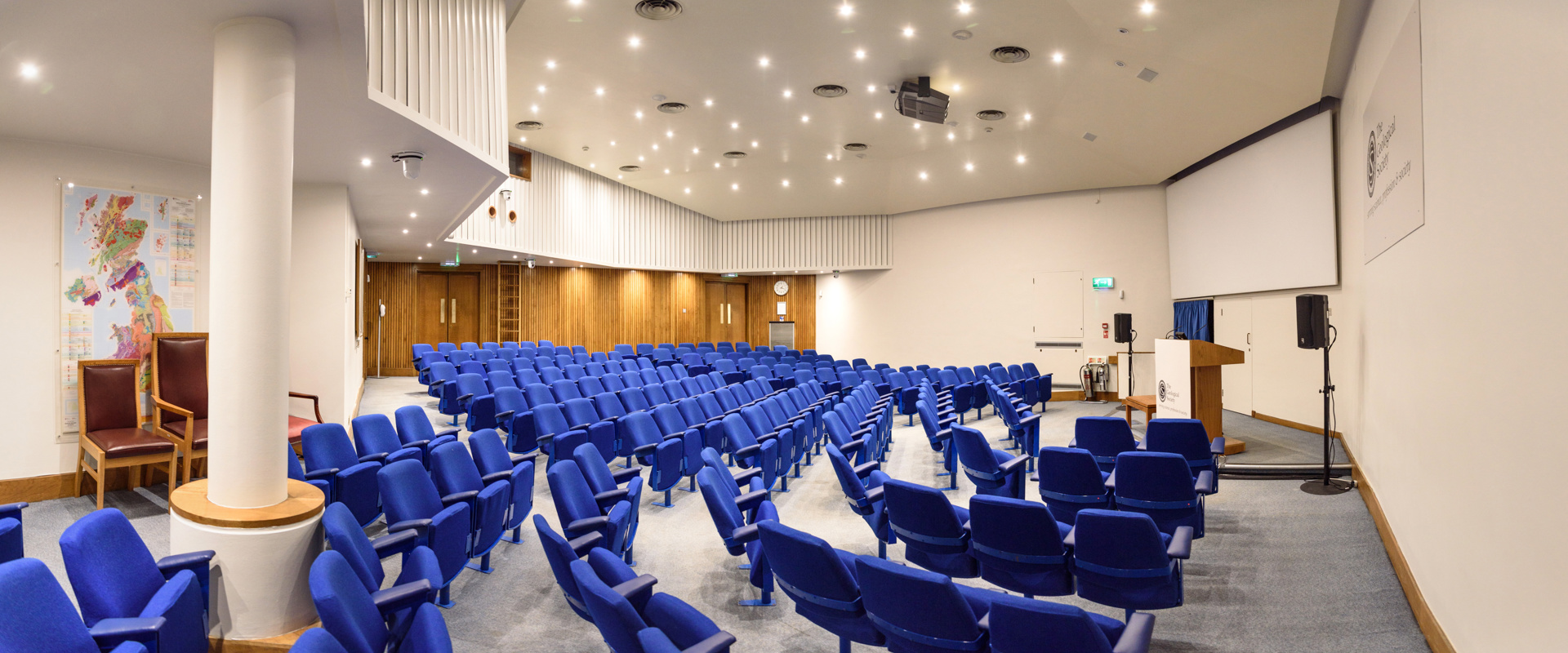 Lecture theatre with blue seating, white walls and a large screen