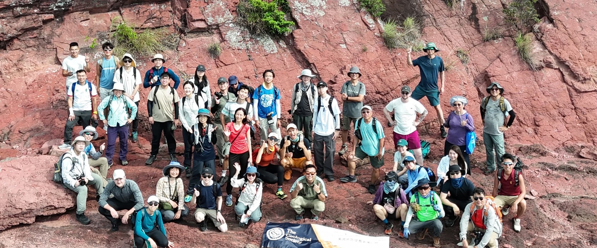 A group of people on standing at the bottom of a rocky cliff with a banner on the ground